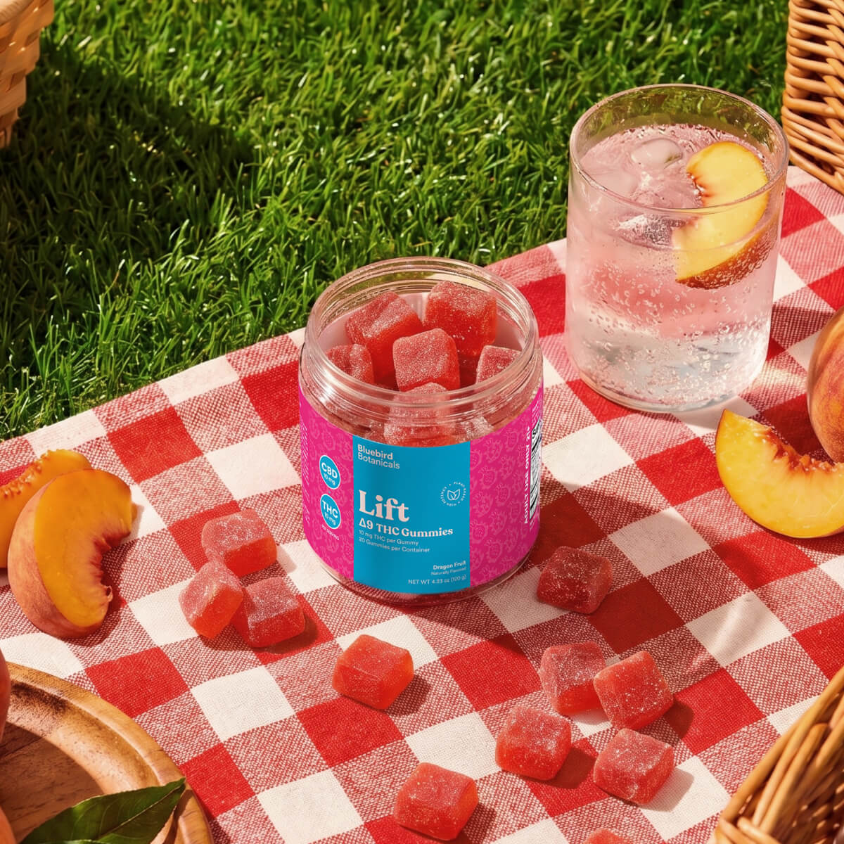 Jar of gummies labeled 'Lift' on a red and white checkered tablecloth with peaches and a glass of water..; Flavor: Dragon Fruit;