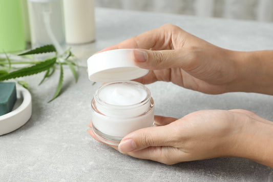Woman holding jar of hemp cream at light table, close-up. Natural cosmetics
