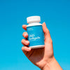 Hand holding a bottle of Bluebird Botanicals 100 mg Broad Spectrum CBD Softgels against a blue background.; Strength: 100 mg;